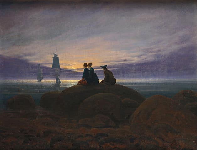 A group of people sitting on a rock looking at a sailboat