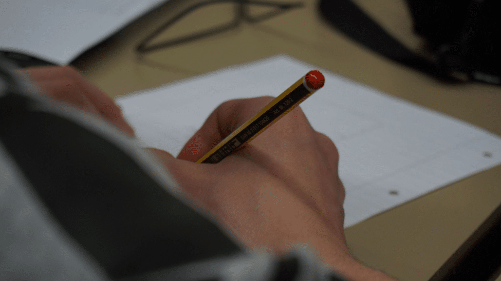 Hand holding a pencil writing on lined paper